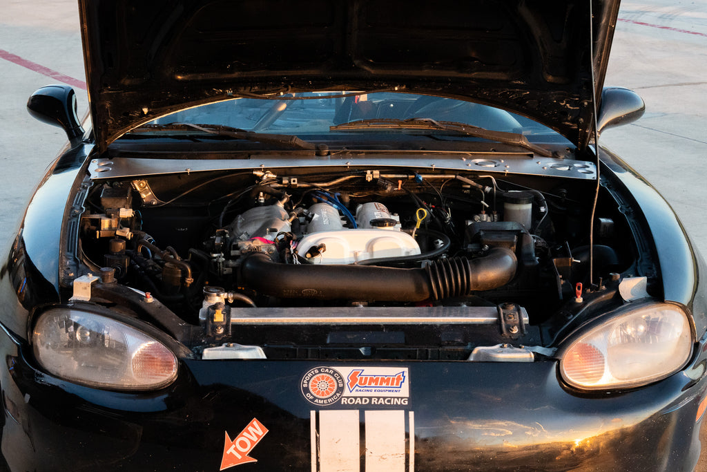 Black car with open hood showing engine details on a road.