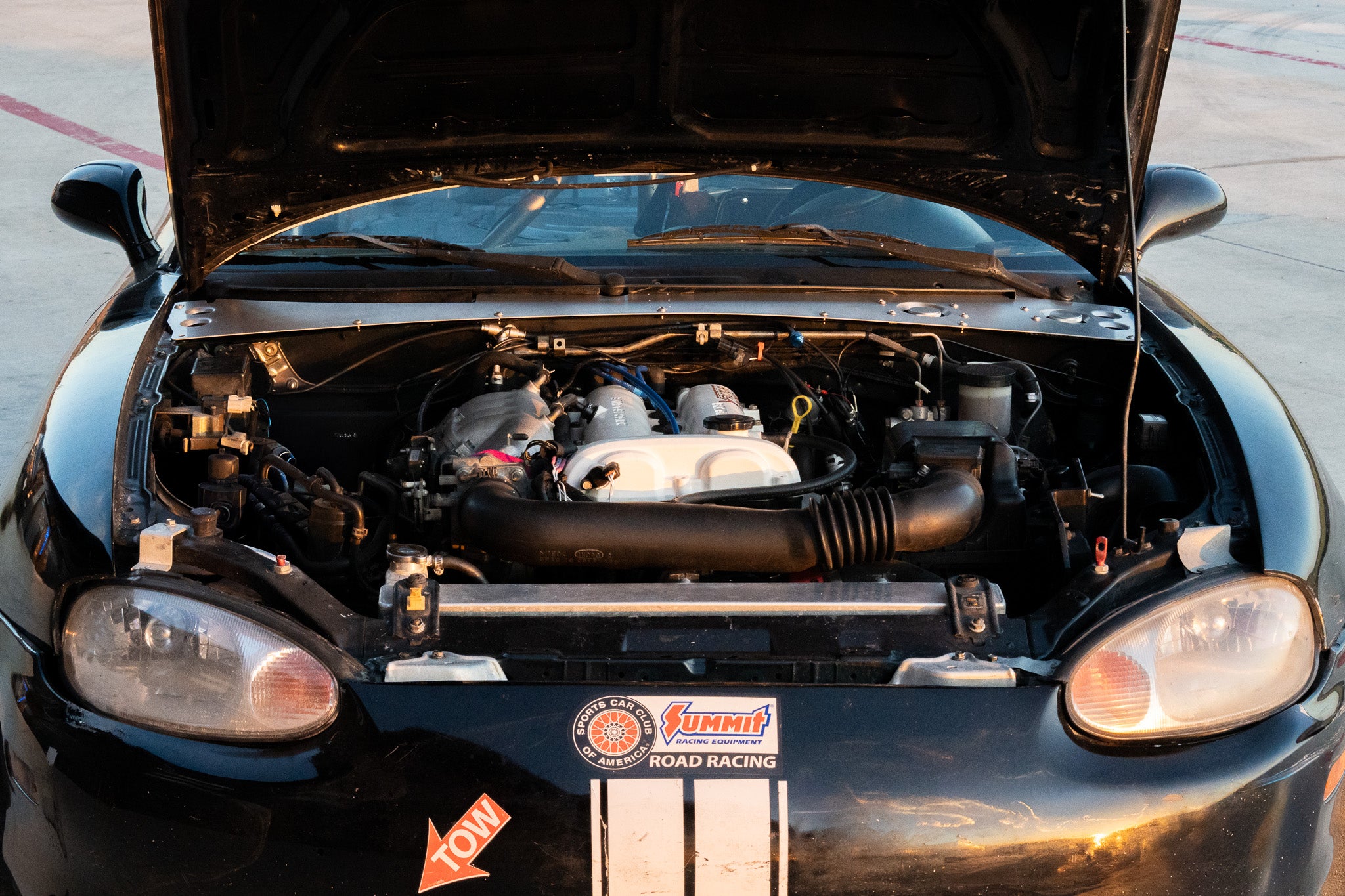 Black car with open hood showing engine details on a road.